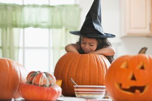 Hispanic girl in witch's hat carving a pumpkin